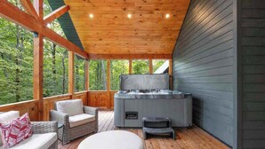 Una terraza de madera con un jacuzzi, muebles de mimbre y vistas al bosque.