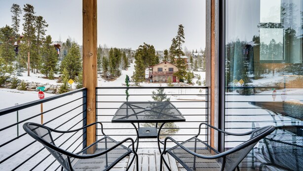 Un balcon avec une table et des chaises, donnant sur un paysage enneigé avec des arbres et un bâtiment.