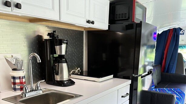 Una cocina compacta con armarios blancos, un refrigerador negro, una cafetera y un lavamanos.
