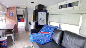 Un espacio habitable pequeño con un sofá, una mesita, un cubo de basura y una alfombra con motivos deportivos.