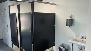 Baño con cabinas separadas en negro, un lavamanos blanco y un cubo de basura.