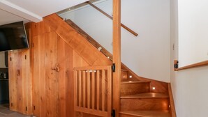 Un escalier en bois avec une rampe en verre, menant à un palier où se trouve un téléviseur à écran plat.