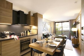 A modern kitchen with a dining area, wooden cabinetry, and a large window providing a view of the outdoors.