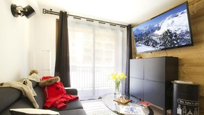 Ein modernes Wohnzimmer mit einer Couch, einem Glastisch, einem an der Wand montierten Fernseher und Blick auf eine verschneite Berglandschaft.