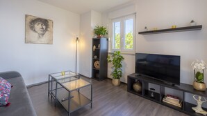A modern living room with a flat-screen TV, a glass coffee table, a sofa, a bookshelf, and a potted plant. - Apartment mit Wunderschönem Meerblick nur 5 Minuten vom Strand Entfernt (Sveta Marina)