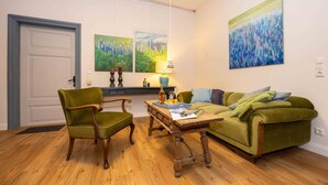A living room with a green sofa, two armchairs, a wooden coffee table, and two paintings on the wall. - Lieblings-ort Lulu - Raum für Zeit (Ludwigslust)