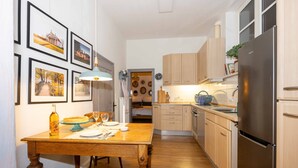 A kitchen with wooden cabinets, a stainless steel refrigerator, a dining table with chairs, and framed pictures on the wall. - Lieblings-ort Lulu - Raum für Zeit (Ludwigslust)