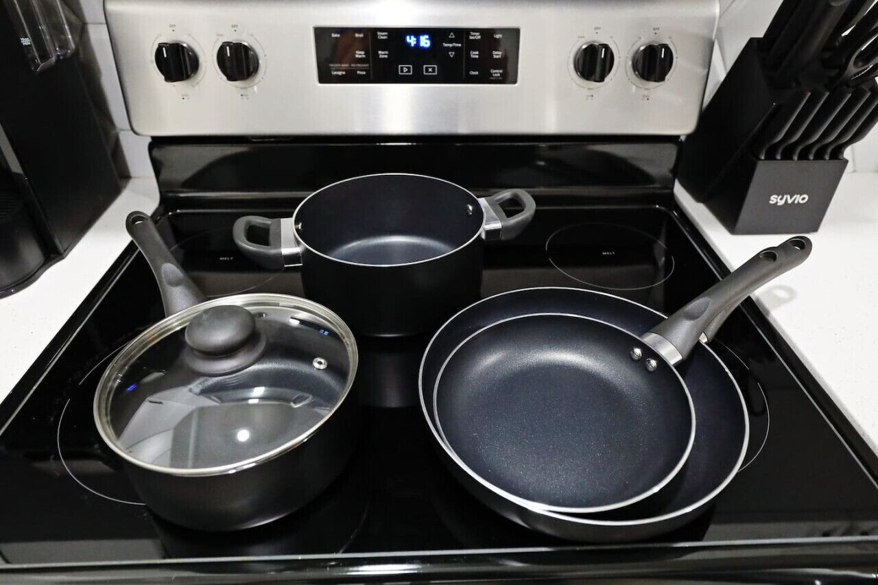 A kitchen with a stove, two pots, and a frying pan.