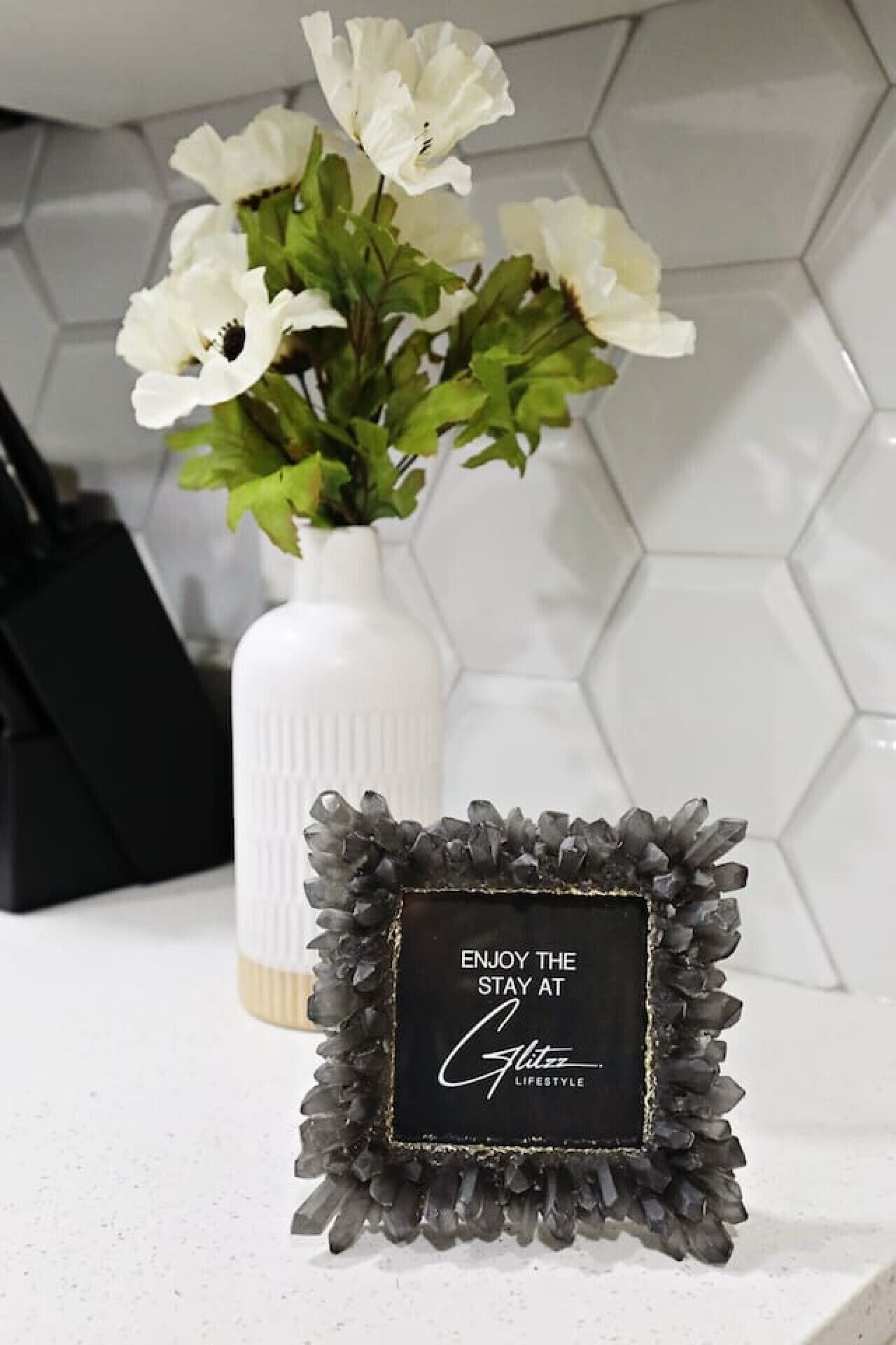 A white vase with white flowers on a white countertop.
