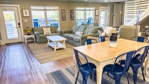 A spacious living area with a wooden floor, a dining table with blue chairs, a green sofa, and a staircase in the background. - L👀K! NEW LISTING! Lakefront; Boat Ramp. Lake Powell! Rent both sides - sleeps 18 (Panama City Beach)