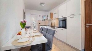 Een moderne keuken met witte kasten, een inbouwoven en een eethoek met een tafel gedekt voor vier personen.