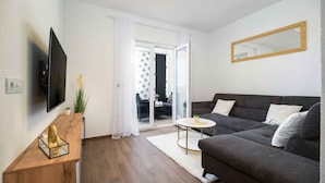 Een moderne woonkamer met een donkergrijze bank, een flatscreen televisie, een houten bijzettafeltje en een ronde salontafel.