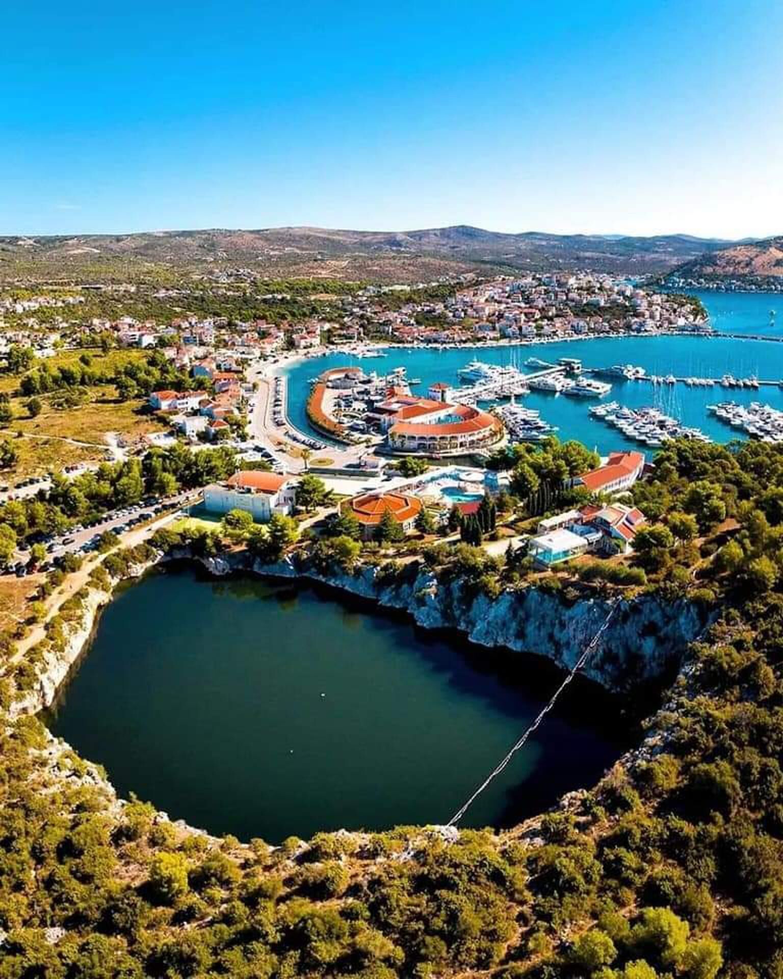 Vue aérienne d’une ville côtière avec un port de plaisance, une vaste étendue d’eau et une végétation luxuriante environnante.