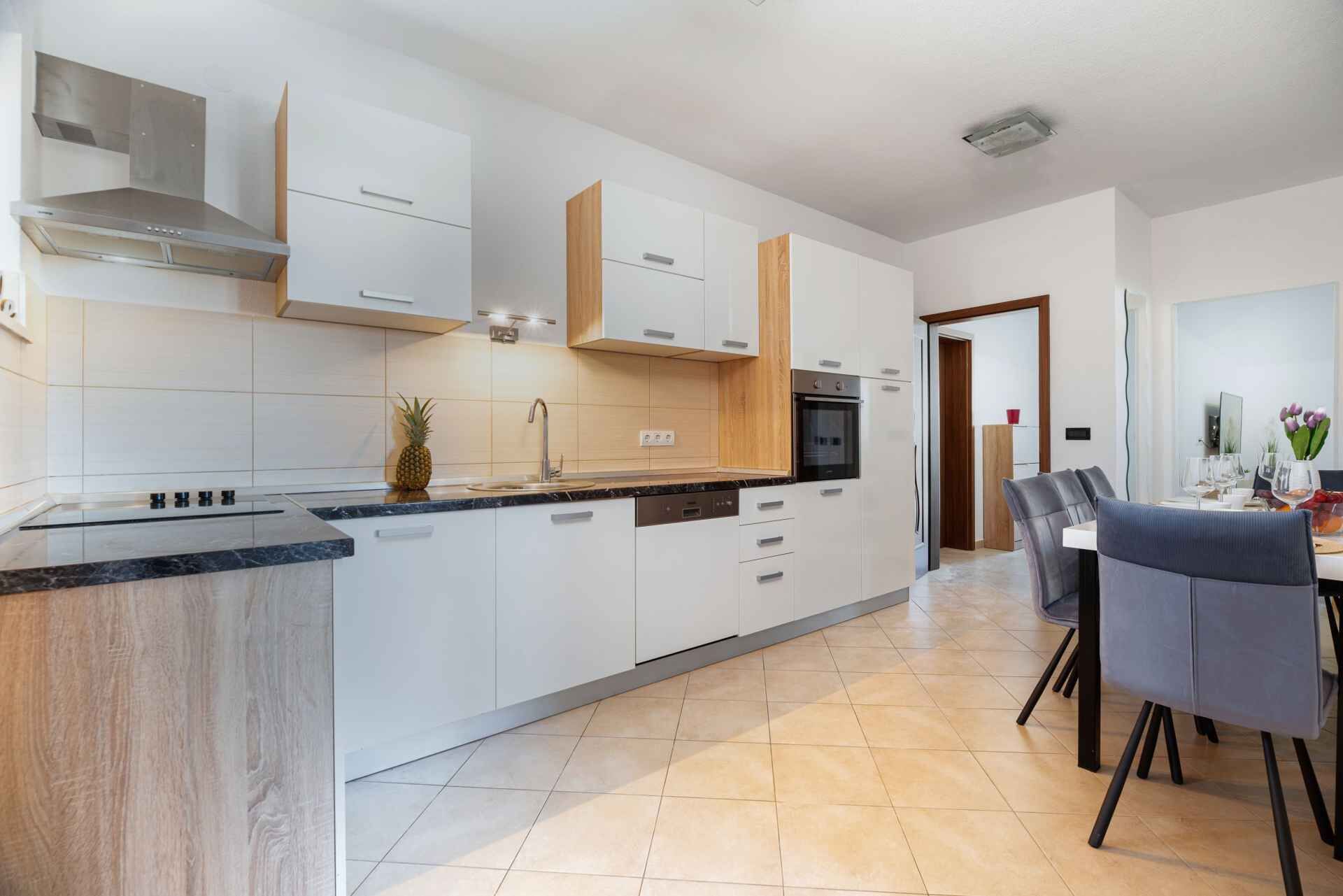 Una cocina moderna con armarios blancos, una isla central y una zona de comedor con mesa y sillas.