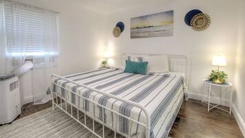 A bedroom with a bed, bedside tables, a ceiling fan, a radiator, and a window with blinds.