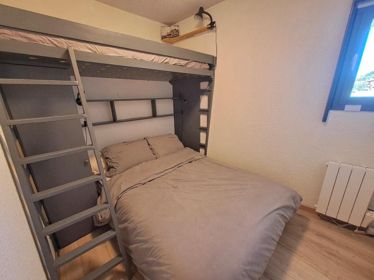 Uma cama beliche com escada, uma cama de solteiro embaixo, um radiador e uma janela com luz do dia.