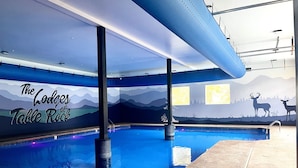 An indoor swimming pool with a mural of mountains and deer, a ceiling with recessed lighting, and a poolside area with a stone floor. - Lodge Near SDC with 4 King Suites and Pools (Branson)