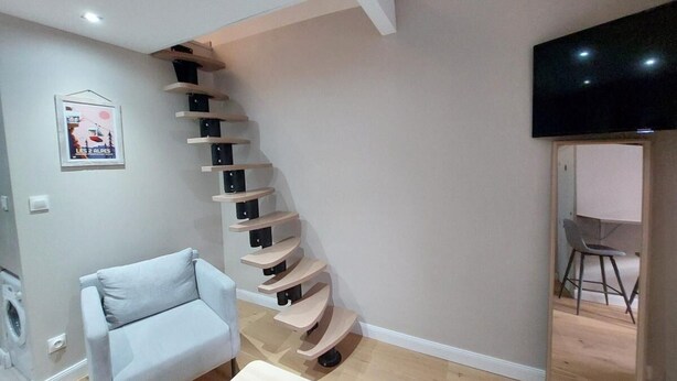 A modern living room with a spiral staircase, a light blue sofa, and a flat-screen TV mounted on the wall.