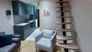 A modern living room with a grey sofa, a light blue armchair, and a wooden coffee table. A spiral staircase leads to an upper level.