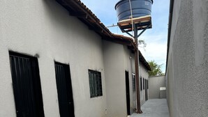 Un estrecho callejón con paredes grises, puertas negras y un tanque de agua a la derecha.