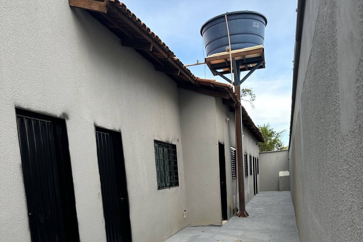 A narrow alleyway with grey walls, black doors, and a water tank on the right.