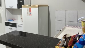 Una cocina con armarios blancos, encimera negra y refrigerador blanco.