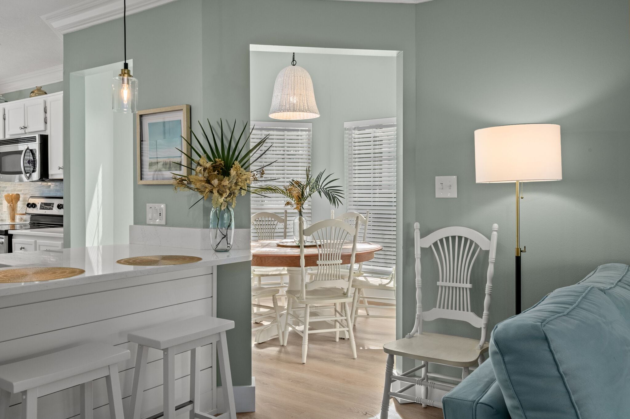 A modern kitchen with white cabinetry, a dining area with white chairs, and a light blue sofa.