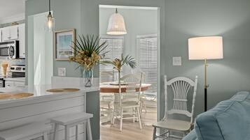 A modern kitchen with white cabinetry, a dining area with white chairs, and a light blue sofa.