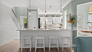 A modern kitchen with white cabinetry, a central island with bar stools, pendant lighting, and a view into the dining area.