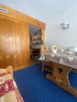 Un comedor de madera con una mesa dispuesta para dos, una alfombra azul estampada y un aparador con estantes.
