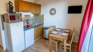 A compact kitchen with a microwave, coffee maker, and dishwasher. There's a sink with a faucet, a dining table with chairs, and a clock on the wall. - 200m from ski slopes, 1st floor, view valley/exceptional, swimming pool, balcony, tv, ski locker (Les Orres)