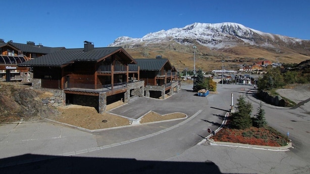 A lodge with a stone facade, wooden balconies, and a view of a snow-capped mountain.
