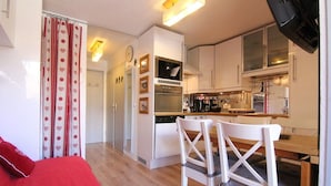 A compact kitchen with white cabinets, a built-in oven, and a dining area with white chairs.