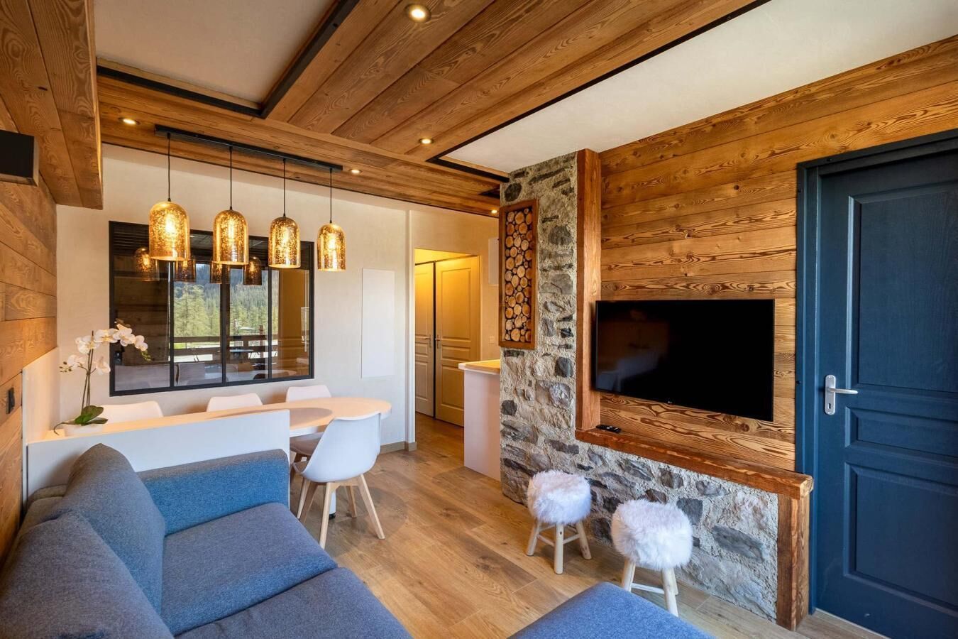 A modern living room with a stone fireplace, wooden ceiling beams, and a large TV mounted on the wall.