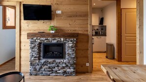 A cozy room with a stone fireplace, wooden panel walls, a flat-screen TV mounted above it, and a small potted plant on the mantel. - 50m from ski slopes, 2nd floor, fitness, swimming pool, sauna, balcony, fireplace or stove, tv (Les Orres)