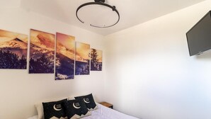 A bedroom with a bed, a nightstand, a flat-screen TV, and a wall-mounted ceiling light. - 50m from ski slopes, 2nd floor, fitness, swimming pool, sauna, balcony, fireplace or stove, tv (Les Orres)