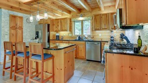 A spacious kitchen with wooden cabinets, a central island with bar stools, a stainless steel refrigerator, and a dishwasher. - Pocono Dog-Friendly Home on River (Damascus)