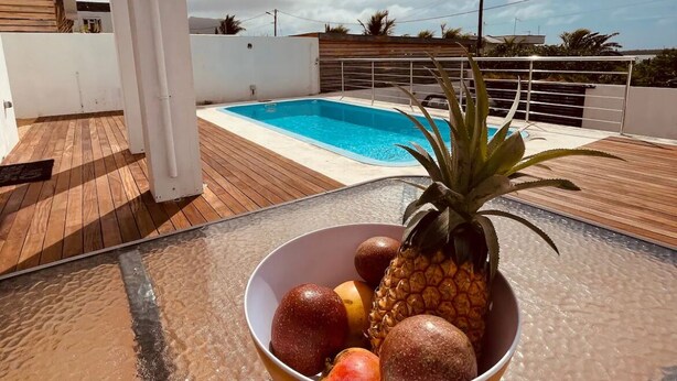 Zona de piscina amb terrassa de fusta, una piscina blanca i un bol de fruita.