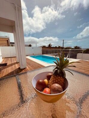 A poolside area with a wooden deck, a white pool, and a bowl of fruit.