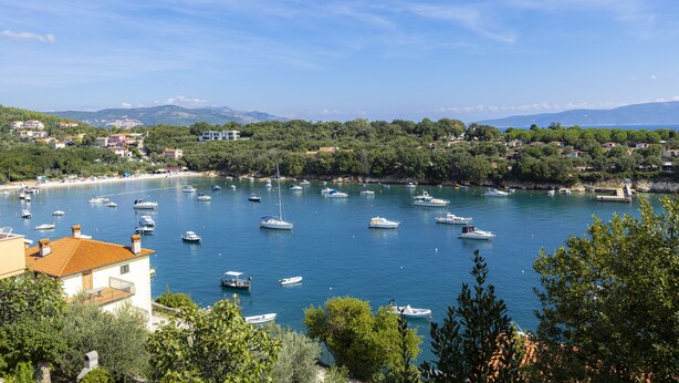 Une ville côtière où des bateaux sont amarrés dans une baie, entourée de verdure et de bâtiments.
