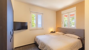 Une chambre avec un lit, un téléviseur fixé au mur et deux fenêtres avec des rideaux.