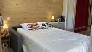 Hotellihuone, jossa on puinen sängynpääty, valkoisilla lakanoiden koristeltu sänky, yöpöytä lampun kanssa ja punainen verho.