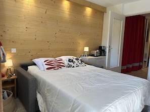 Habitación de hotel con cabecera de madera, cama con ropa de cama blanca, mesita de noche con lámpara y cortina roja.