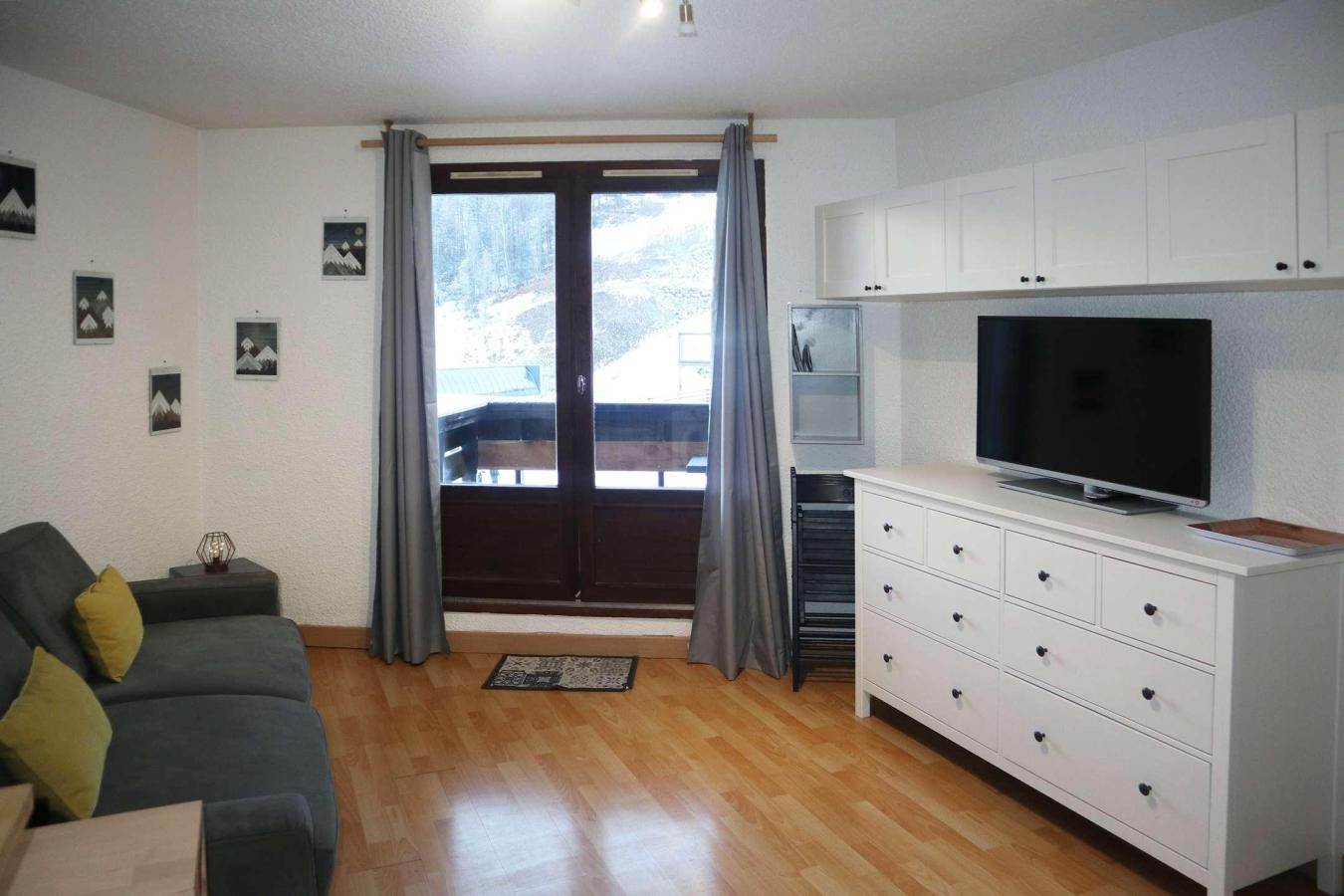 A living room with a sofa, a TV, a white cabinet, and a view of a snowy landscape through a sliding door.