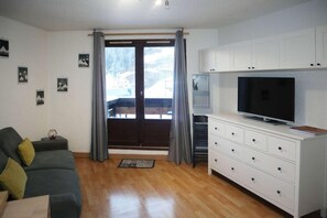 A living room with a sofa, a television on a cabinet, a window with curtains, and a view of a snowy landscape.