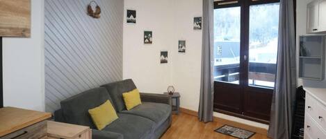 Una sala de estar con un sofá gris, piso de madera, una mesita y una ventana con cortinas.