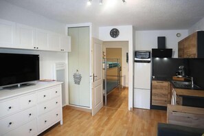 A compact kitchen with white cabinets, a built-in TV, a microwave, and a sink.