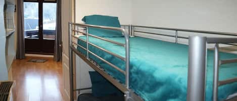 Ein Etagenbett mit einer türkisblauen Matratze in einem Zimmer mit Holzboden und einer Tür zu einem Außenbereich.