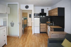 A compact kitchen with a microwave, stove, and sink, a small dining area with a table and chairs, and a door leading to a hallway.