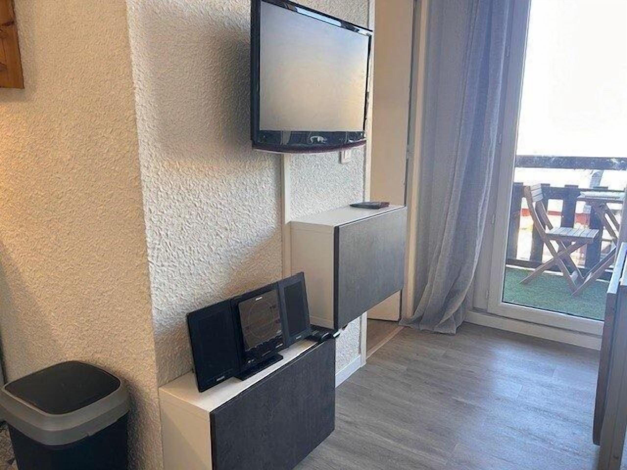 Een moderne woonkamer met een flatscreen televisie aan de muur, een klein tafeltje met een afstandsbediening en een prullenbak.